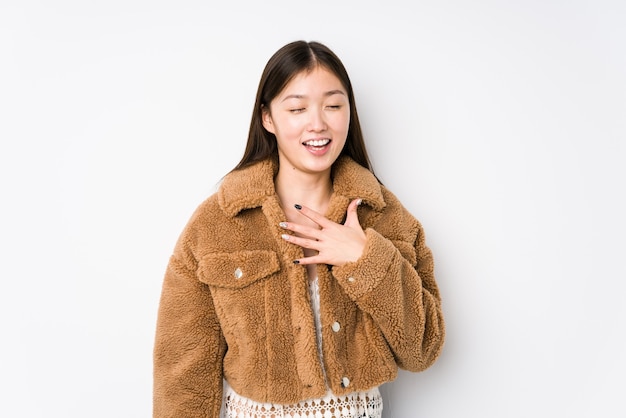 Young chinese woman posing in a white background isolated laughs out loudly keeping hand on chest.