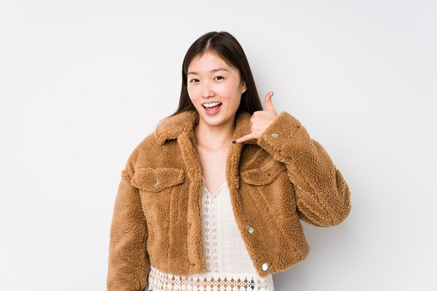 Young chinese woman posing in a white  isolated showing a mobile phone call gesture with fingers.