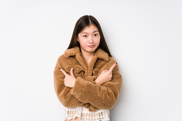 Young chinese woman posing in a white wall points sideways, is trying to choose between two options.