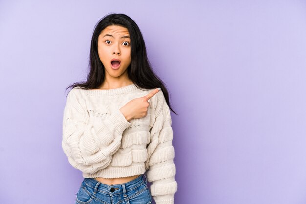 Young chinese woman on a purple wall pointing to the side