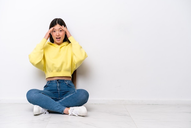 Young Chinese woman sitting on the floor isolated on white wall with surprise expression