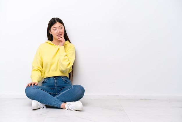 사진 흰 벽에 고립된 바닥에 앉아 올려다보는 동안 아이디어를 생각하는 젊은 중국 여성