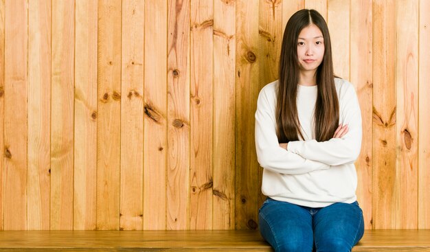 Young chinese woman sitting on a wooden place unhappy looking in camera with sarcastic expression.