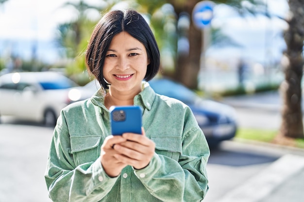 Photo young chinese woman smiling confident using smartphone at street