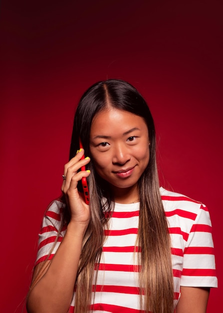 Young chinese woman smiling and talking on smartphone while standing on red background