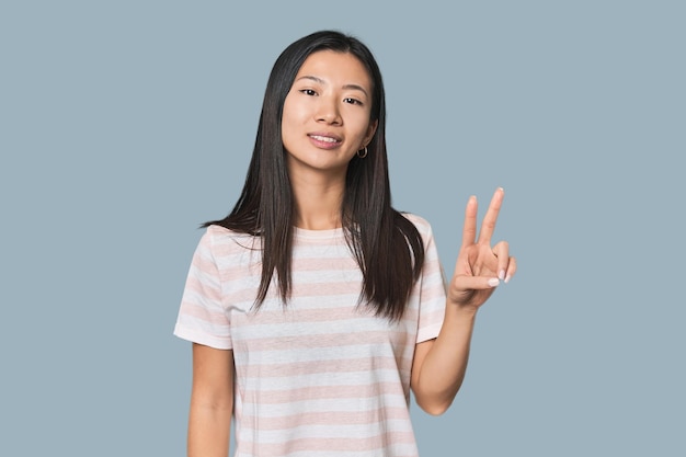 Young Chinese woman in studio setting showing victory sign and smiling broadly