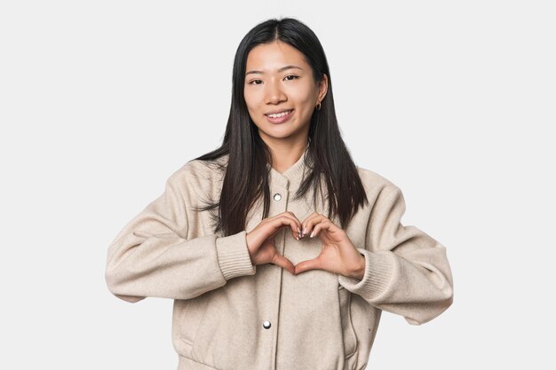 Photo young chinese woman in studio setting smiling and showing a heart shape with hands