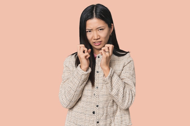 Young Chinese woman in studio setting upset screaming with tense hands