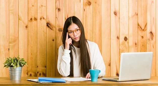 Young chinese woman studying on her desk pointing temple with finger