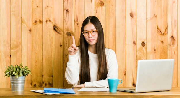 Young chinese woman studying on her desk showing number one with finger.