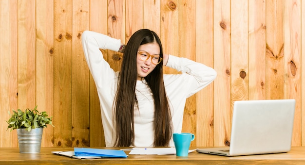 Young chinese woman studying on her desk stretching arms, relaxed position.