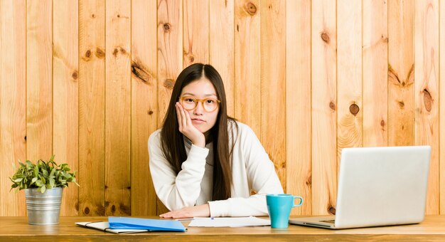 退屈して、疲れていて、リラックスした一日が必要な彼女の机で勉強している若い中国人女性。