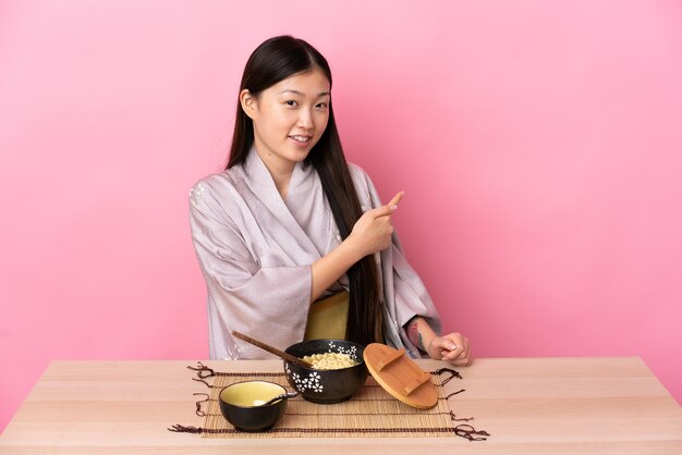 Young Chinese woman wearing kimono and eating noodles pointing back