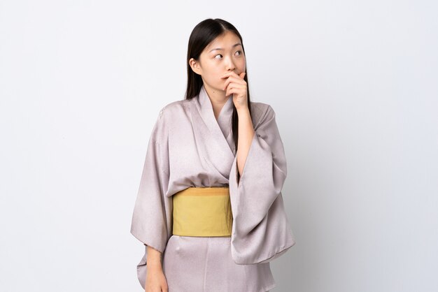 Young Chinese woman wearing kimono over isolated wall having doubts and with confuse face expression