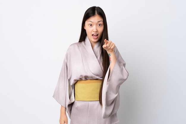 Young Chinese woman wearing kimono over isolated wall surprised and pointing front