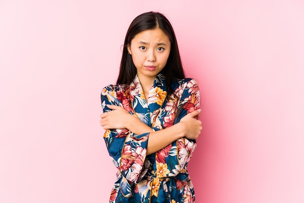 Young chinese woman wearing a kimono pajama isolated going cold due to low temperature or a sickness.