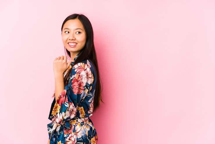 Photo young chinese woman wearing a kimono pajama isolated points with thumb finger away, laughing and carefree.