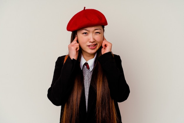 Foto giovane donna cinese che indossa un'uniforme scolastica isolata sulle orecchie bianche della copertura con le mani.