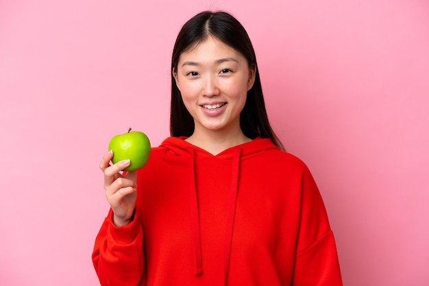 Young Chinese woman with an apple isolated on pink background smiling a lot