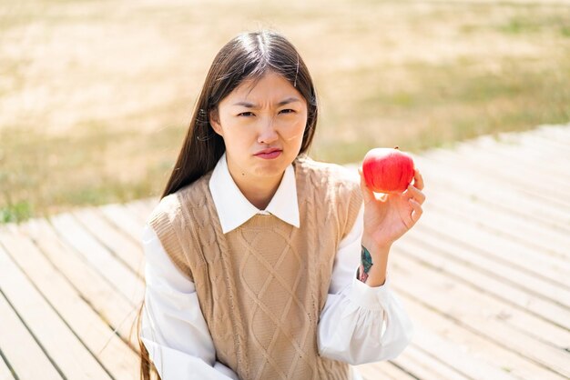 悲しい表情で屋外でリンゴを持つ若い中国人女性