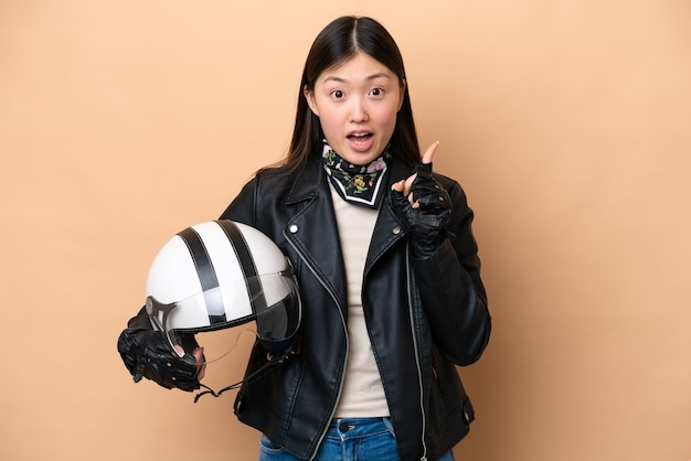 Young Chinese woman with a motorcycle helmet isolated on beige background intending to realizes the solution while lifting a finger up