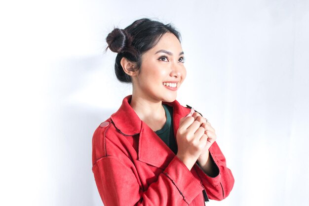 Young chinese woman with praying gesture wishing you good luck with happy and smile face Indonesian woman on gray background