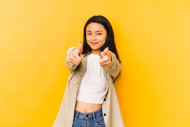 Young chinese woman on a yellow wall with thumbs ups, cheers about something