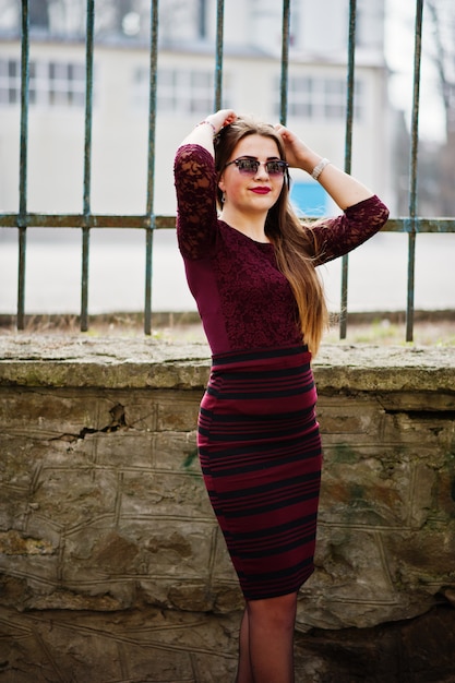 Young chubby teenage girl wear on red dress with sunglasses posed against iron fence.