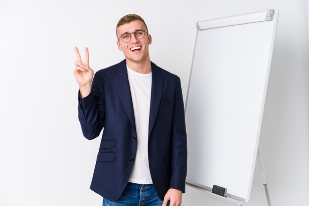 Young coaching man showing a white board joyful and carefree showing a peace symbol with fingers.