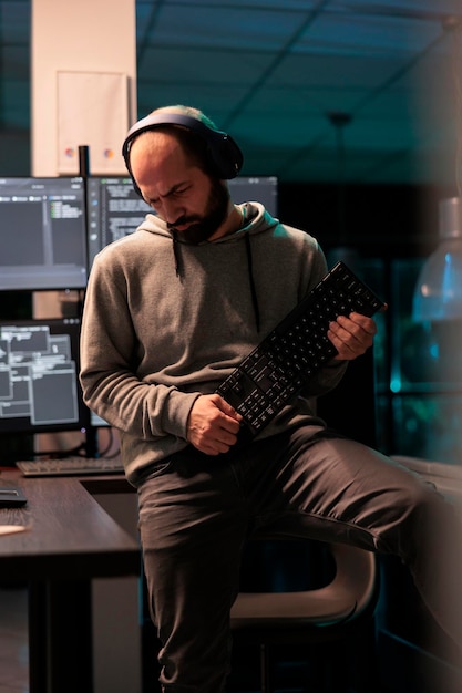 Young coder fooling around with keyboard playing guitar, working on user interface with multiple screens parsing algorithm in software agency. Writing code and programming server.