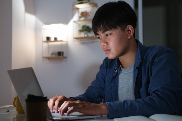 Young collage man learning online at night at his home.