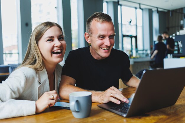 Young colleagues managers are sitting at the table and laughing concept of business cooperation and teamwork young smiling people at the table in the office with a laptop modern successful people