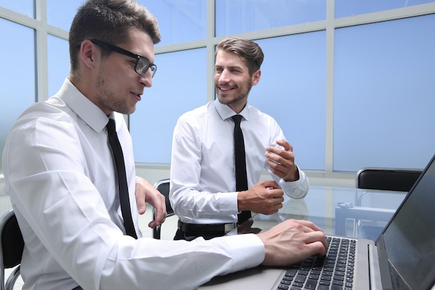 Young colleagues sit at the desk in the office and work on laptops