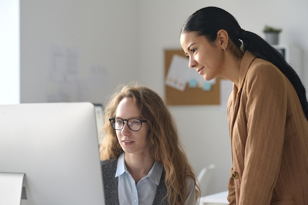 Young colleagues using computer at their online work while working together in office