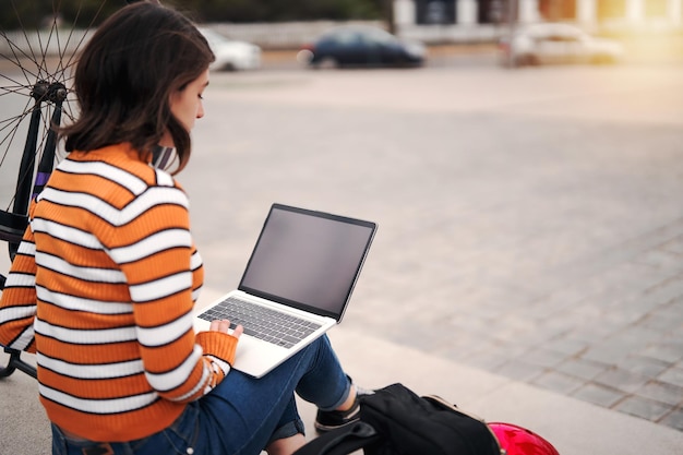 Young college woman with a laptop and bicycle on a step working top viewx9