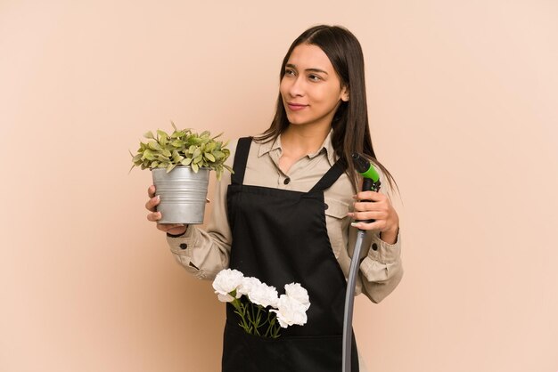 Young Colombian gardener holds a plant and hose, nurturing nature.