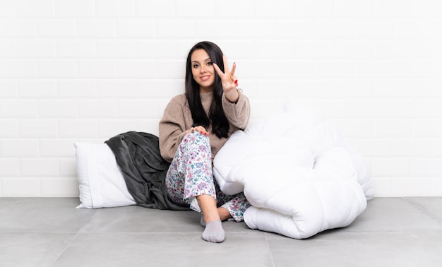 Young Colombian girl in pajamas at indoors happy and counting three with fingers