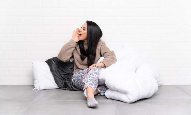 Young Colombian girl in pajamas at indoors shouting with mouth wide open to the lateral