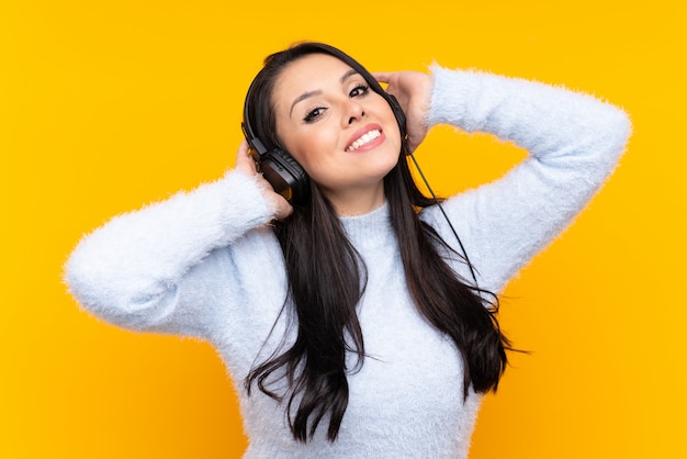 Young Colombian girl over yellow wall listening music