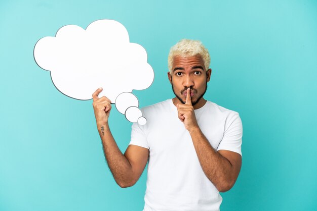 Young Colombian handsome man isolated on blue background holding a thinking speech bubble and doing silence gesture