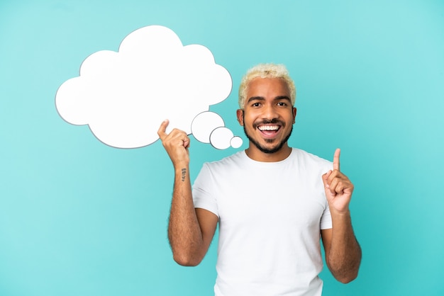 Young Colombian handsome man isolated on blue background holding a thinking speech bubble