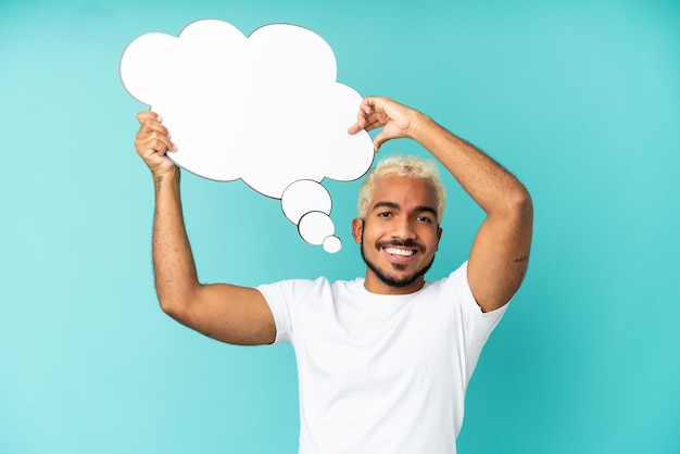 Young Colombian handsome man isolated on blue background holding a thinking speech bubble