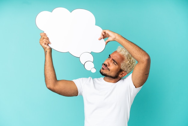 Young Colombian handsome man isolated on blue background holding a thinking speech bubble