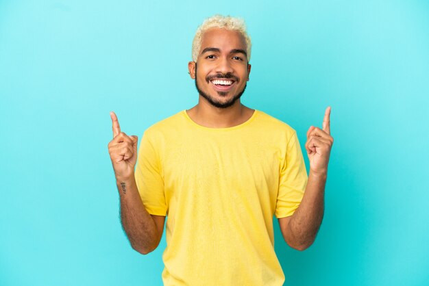 Young Colombian handsome man isolated on blue background pointing up a great idea