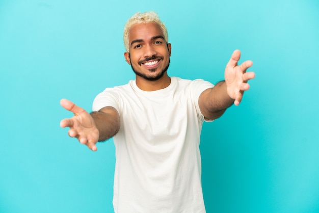 Young Colombian handsome man isolated on blue background presenting and inviting to come with hand