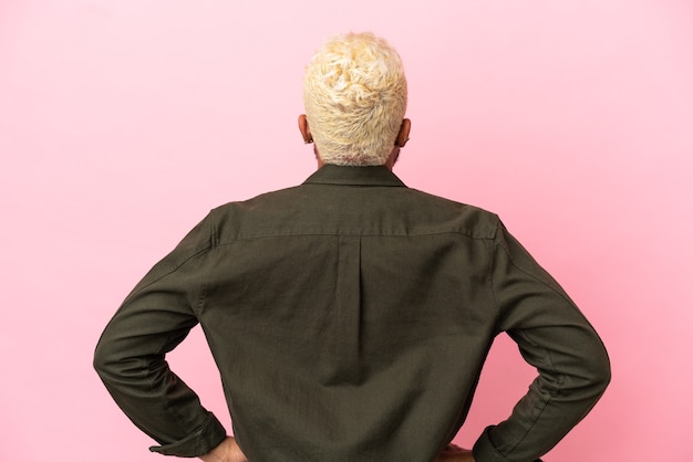 Young Colombian handsome man isolated on pink background in back position