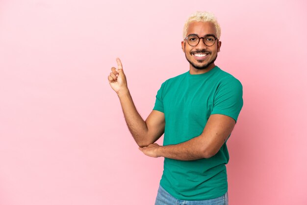 Young Colombian handsome man isolated on pink background happy and pointing up
