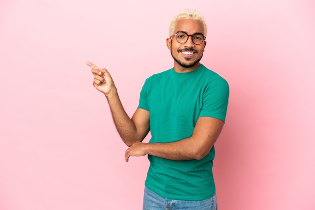 Young Colombian handsome man isolated on pink background pointing finger to the side