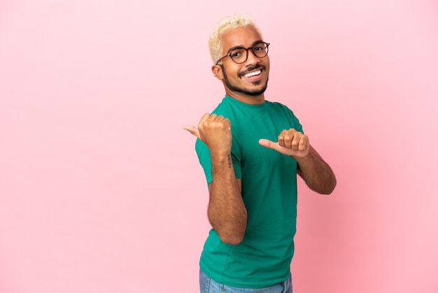 Young Colombian handsome man isolated on pink background pointing to the side to present a product