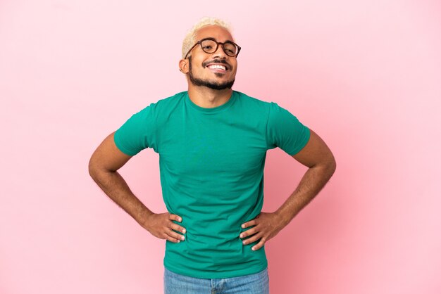 Young Colombian handsome man isolated on pink background posing with arms at hip and smiling